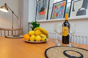A dining table with a plate of fruit, a bottle of wine, and two glasses.