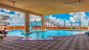 Una piscina con tobogán de agua, palmeras y cielo despejado.