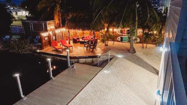 A nighttime view of a beachside patio with wooden deck seating and a pool. - SOUTHERN SUNSET - As seen on House Hunters-S228 E6 - Family Time in the FL Keys (Cudjoe Key)
