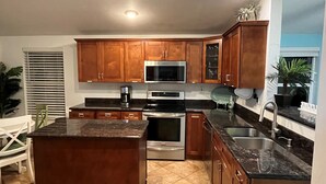 A modern kitchen with wooden cabinets, stainless steel appliances, and a granite countertop. - SOUTHERN SUNSET - As seen on House Hunters-S228 E6 - Family Time in the FL Keys (Cudjoe Key)
