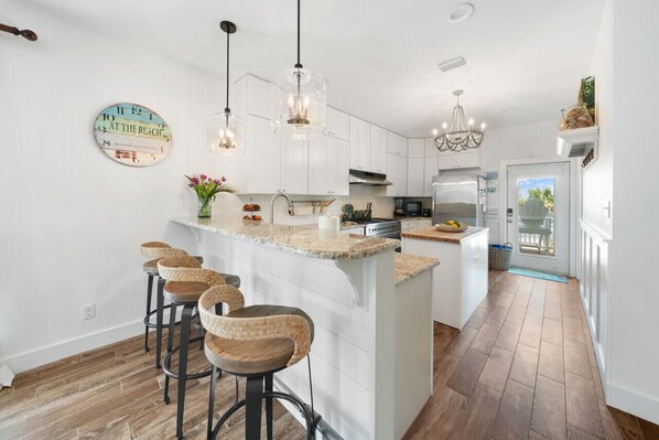 A modern kitchen with white cabinets, a central island with bar stools, pendant lights, and a clock on the wall.