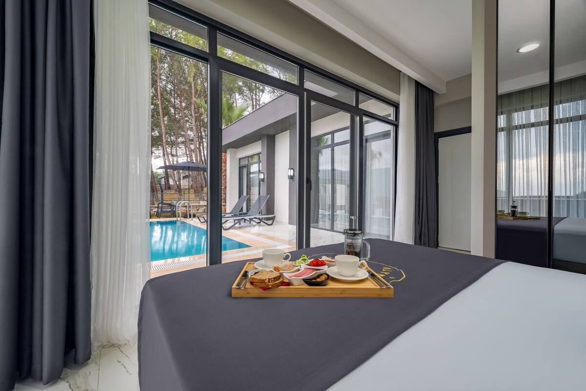 Ein Hotelzimmer mit einem großen Bett, einem Frühstückswagen mit Speisen und Getränken sowie Blick auf einen Außenpool.