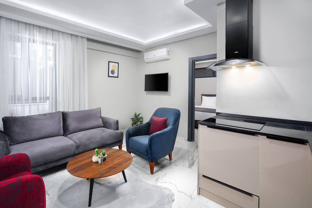 Ein modernes Wohnzimmer mit Sofa, Sessel, Couchtisch und Küchenzeile mit Herd.