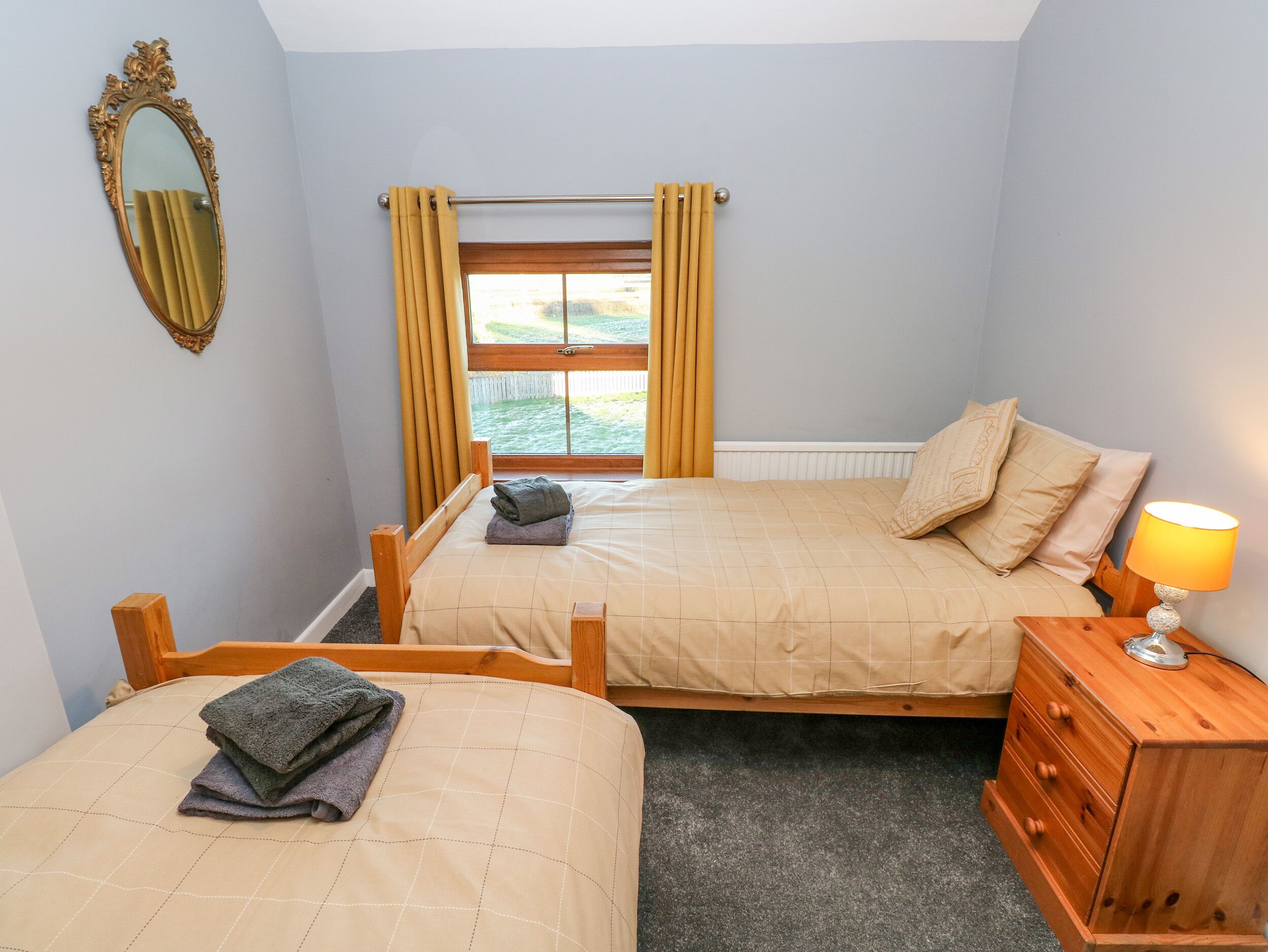 A bedroom with two beds, a wooden dresser, a lamp, and a window with curtains.