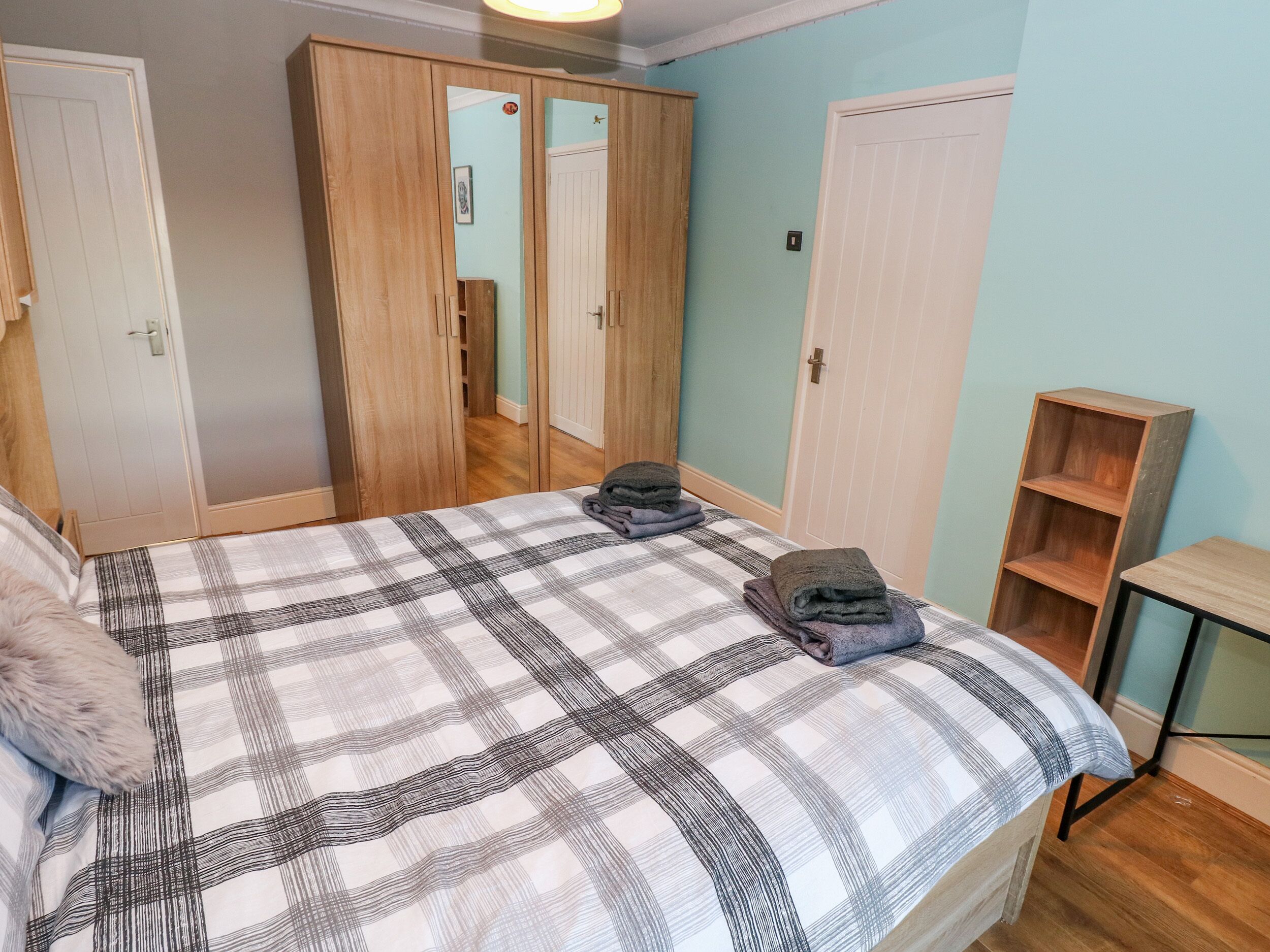 A bedroom with a bed, two wardrobes, a small wooden shelf, and a nightstand.