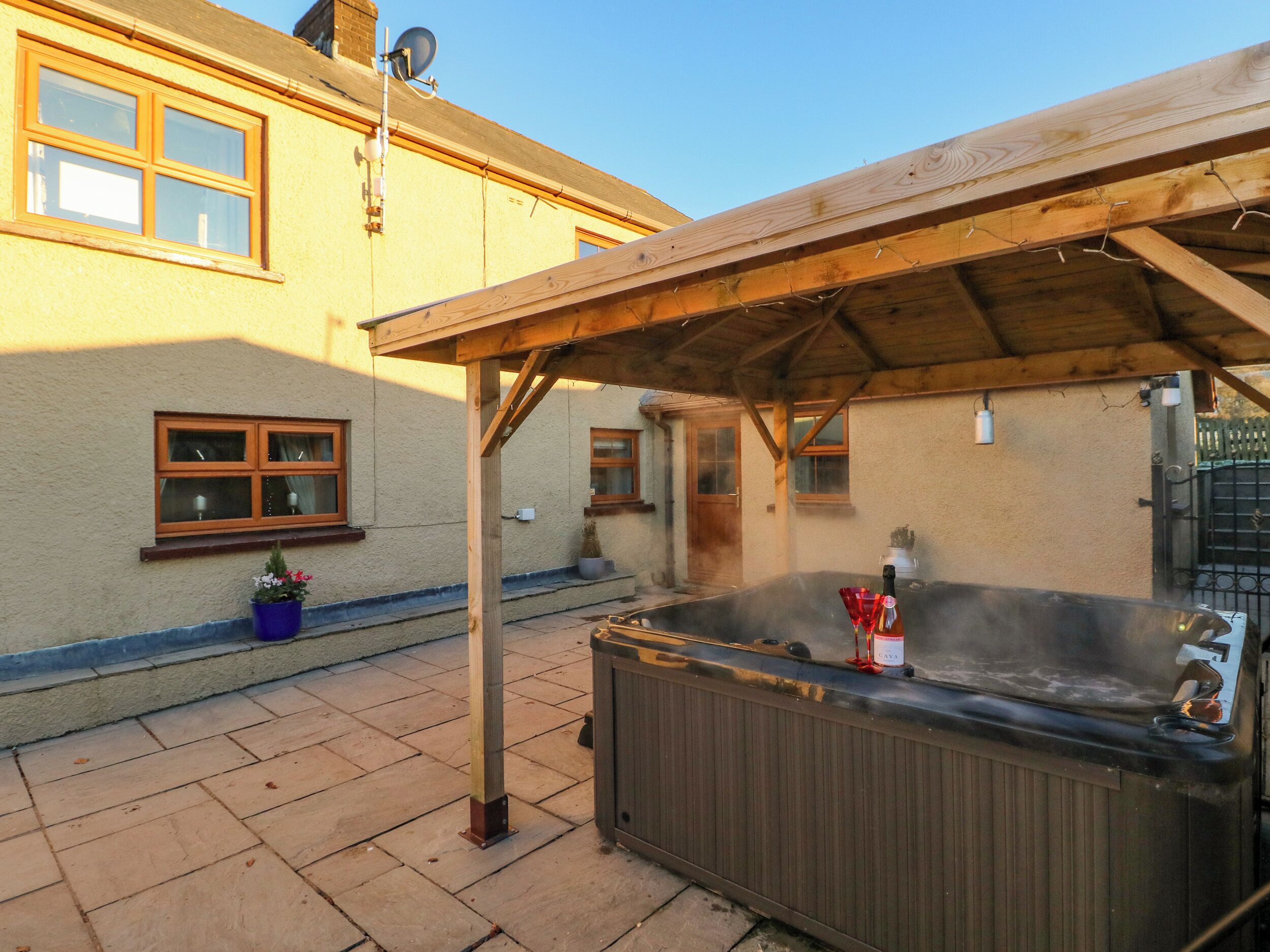 Ein Whirlpool unter einer Holzpergola in einem Innenhof, mit einem Haus im Hintergrund.