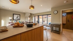 A modern kitchen with a large island, wooden cabinetry, pendant lighting, and a view to the outside. - Hayloft, Burnham Market, Norfolk (Burnham Market)