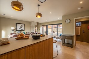 Une cuisine moderne dotée d’un grand îlot central, de meubles en bois, de luminaires suspendus et offrant une vue sur l’extérieur.