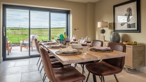 A dining area with a large table set for six, a view of a green landscape through a sliding glass door, and a framed owl artwork on the wall. - Hayloft, Burnham Market, Norfolk (Burnham Market)