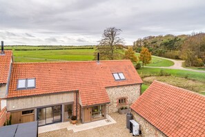 A modern house with a red-tiled roof, large windows, and a view of a green field.