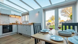 Une cuisine moderne avec des meubles blancs, un plan de travail en bois et un coin repas avec une table dressée pour deux personnes.