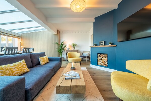A modern living room with a blue accent wall, a fireplace, and a large window. - Golf Cottage, West Runton, Norfolk (West Runton)
