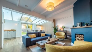 Un salon moderne avec un canapé, des fauteuils et une table basse. On y trouve une cheminée avec un manteau de cheminée et une grande fenêtre qui laisse entrer la lumière naturelle.