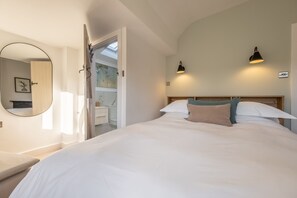 A bedroom with a large bed, a round mirror, two wall-mounted lamps, and a skylight. - Golf Cottage, West Runton, Norfolk (West Runton)