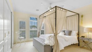 Una cama con dosel, una mesita de noche, una silla y una ventana con persianas.