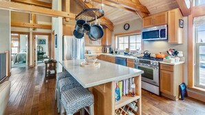 A spacious kitchen with wooden beams, a central island, a stove, and a microwave. - The Lodges D-1 - 1 Block to the Beach! (Cannon Beach)