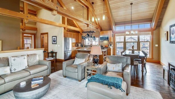 A spacious living room with a high ceiling, wooden beams, a fireplace, and a view of the kitchen and dining area. - The Lodges D-1 - 1 Block to the Beach! (Cannon Beach)