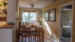 A cozy room with a dining table and chairs, a bed with a floral bedspread, and a window with blinds. - Pet-friendly Cottage in the Trees - GREAT location! (Fernandina Beach)