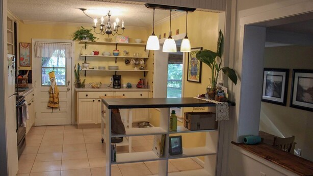 A kitchen with a central island, pendant lights, and a variety of kitchenware on shelves. - Pet-friendly Cottage in the Trees - GREAT location! (Fernandina Beach)