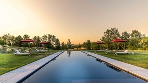 Una piscina all'aperto tranquilla con lettini e ombrelloni rossi, immersa nel verde e alberi.