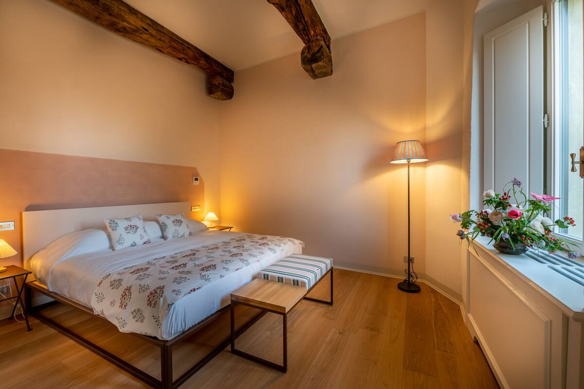 Une chambre à coucher avec un lit, des tables de chevet, une lampe sur pied et une fenêtre décorée de fleurs.