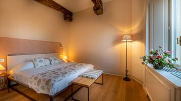 Un dormitorio con cama, mesitas de noche, una lámpara de pie y una ventana con flores.