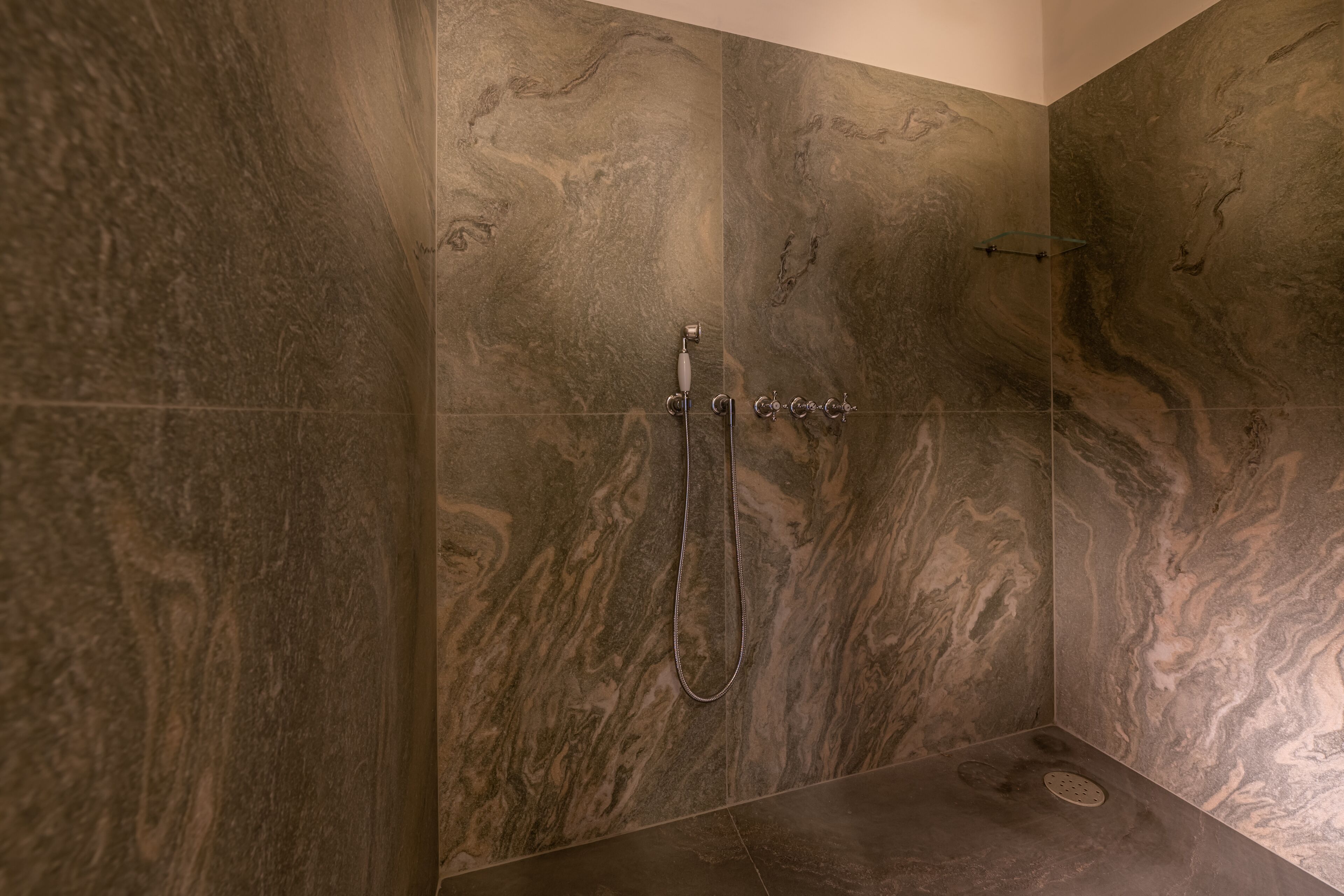 A shower with a handheld showerhead and a wall-mounted faucet.