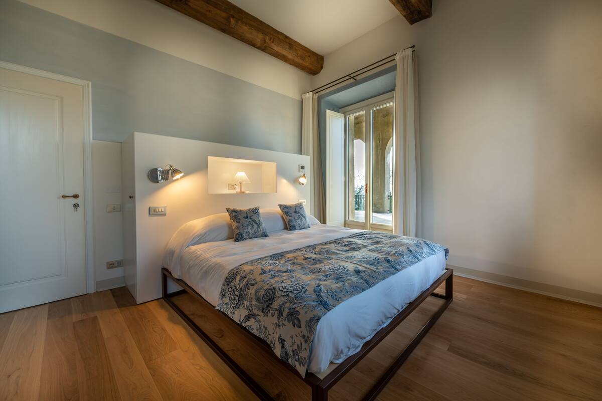 Une chambre à coucher avec un cadre de lit en bois, une grande fenêtre avec des rideaux et un luminaire fixé au mur.