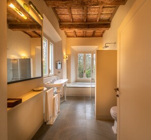 A modern bathroom with a wooden ceiling, a large mirror, a sink, a bathtub, and a toilet.