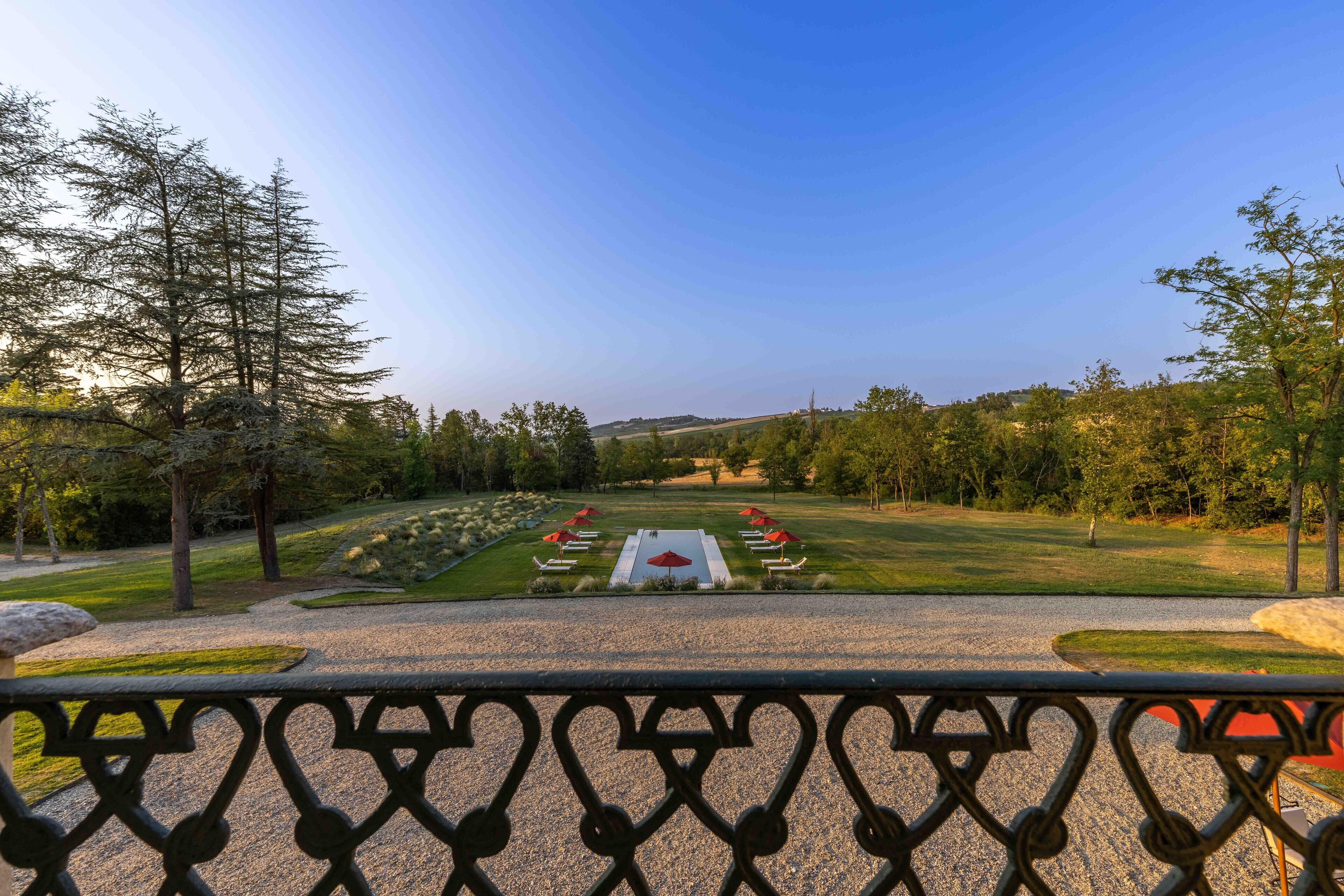 A view from a balcony overlooking a landscaped garden with a central pathway, surrounded by trees and red umbrellas.