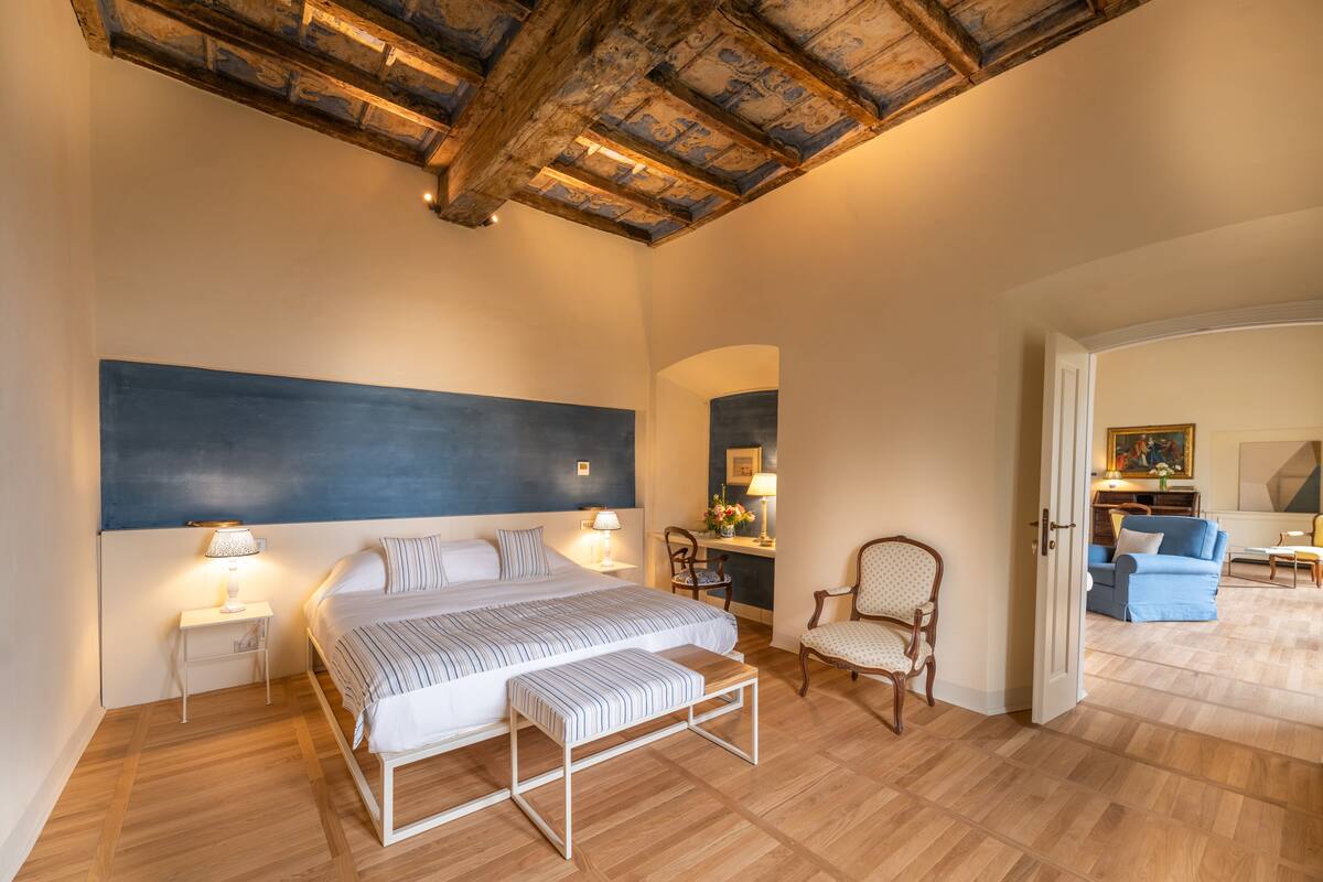 Une chambre à coucher comprenant un lit, des tables de chevet, une chaise et un bureau avec une lampe.