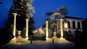 Un'imponente ingresso con colonne classiche, un viale delimitato da un cancello e un edificio con finestre ad arco.