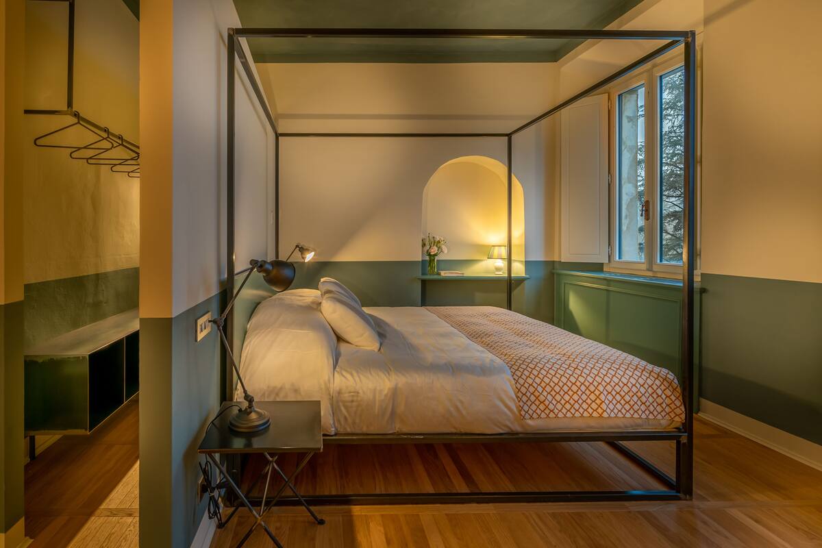 Une chambre à coucher moderne, avec un lit, une lampe de chevet et une fenêtre donnant sur des arbres.