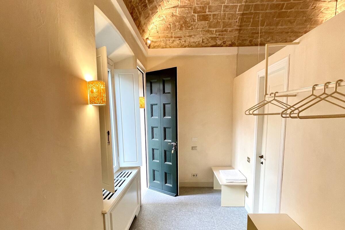 Un couloir étroit avec un plafond en pierre, une porte, un radiateur et un petit coin salon.