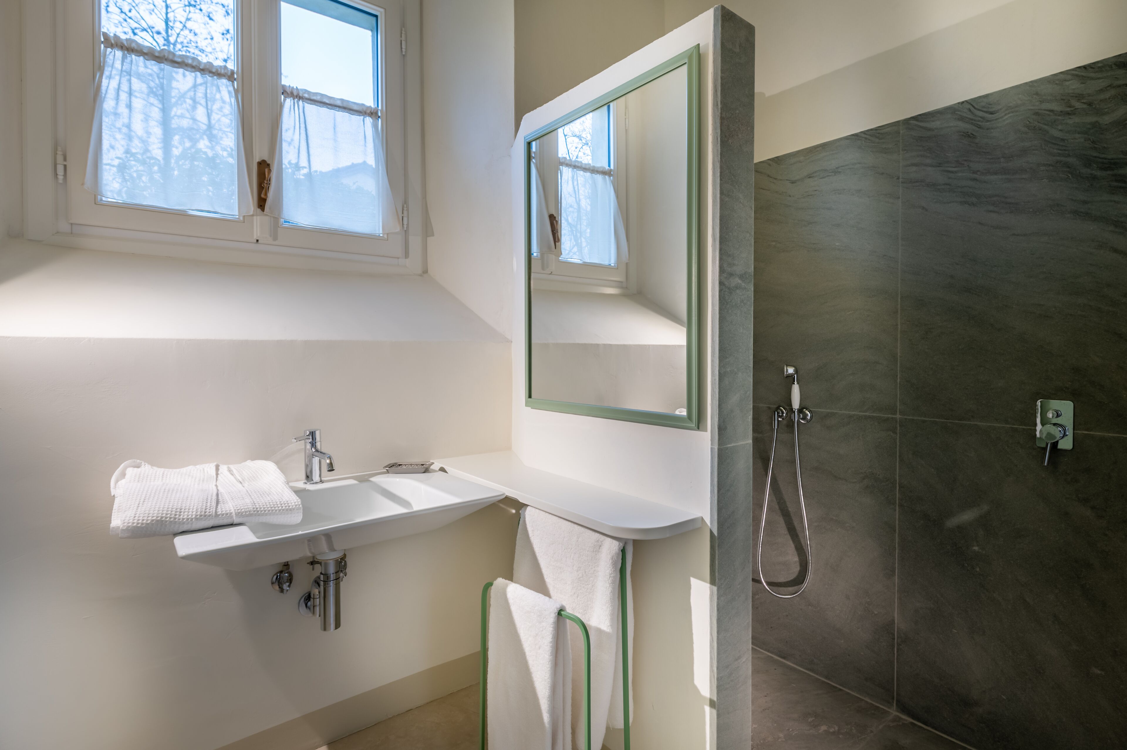 A modern bathroom with a white sink, a towel rack, a mirror, and a shower area.