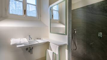 A modern bathroom with a white sink, a towel rack, a mirror, and a shower area.