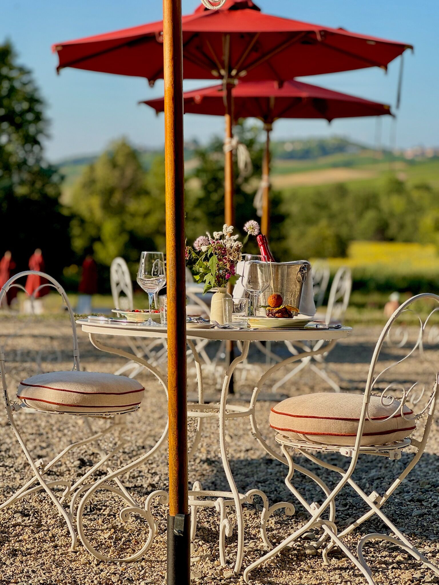 An outdoor dining area with metal chairs and a table set with wine glasses, plates, and a vase of flowers.