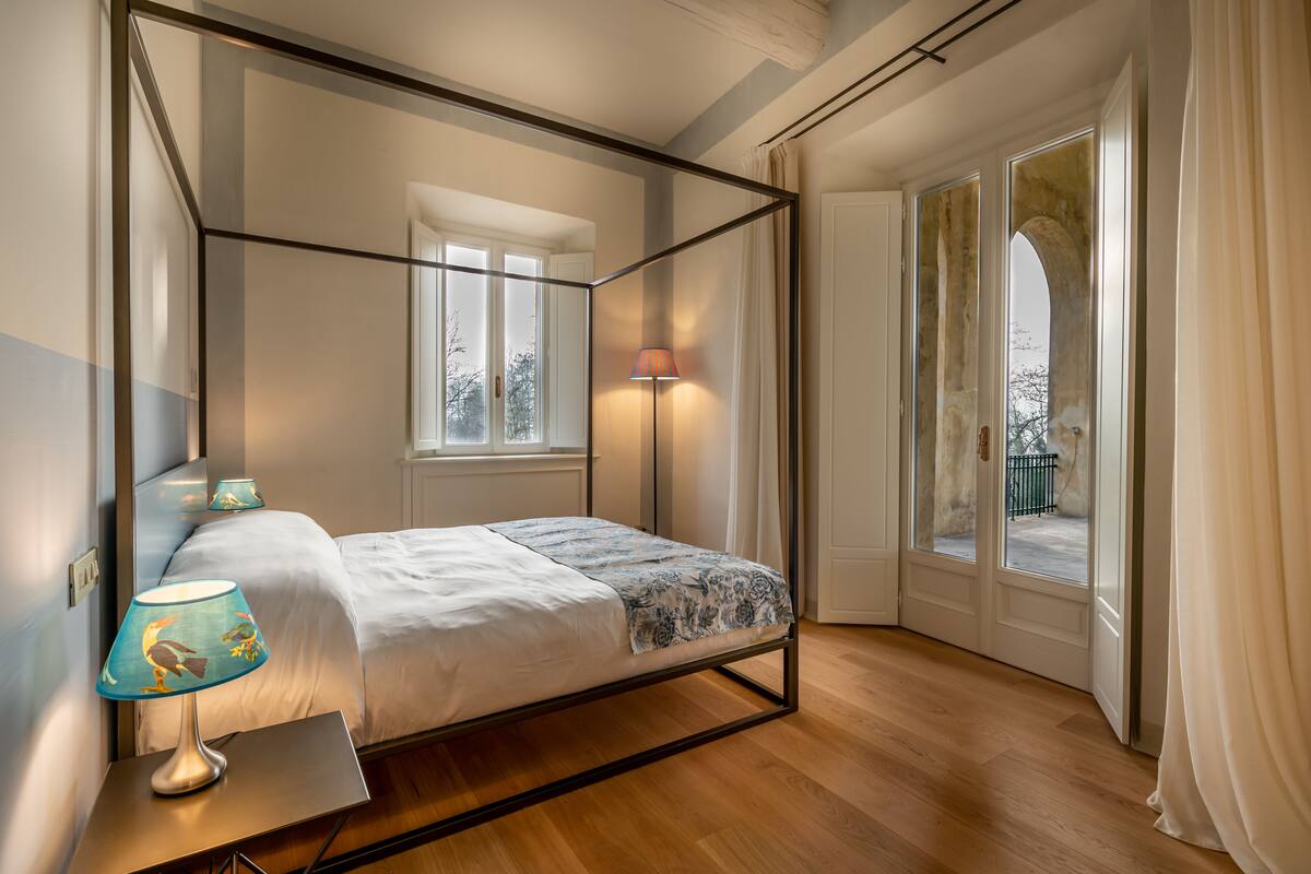 Une chambre à coucher avec un lit à baldaquin, une lampe de chevet, une fenêtre avec des rideaux et une vue sur l’extérieur.