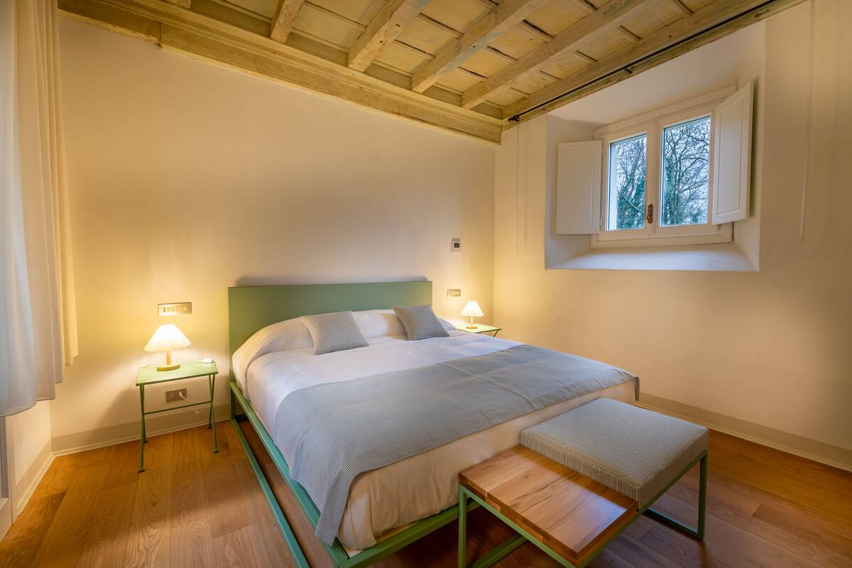 Une chambre à coucher comprenant un lit, des tables de chevet, un banc, une fenêtre et un plafond en bois.