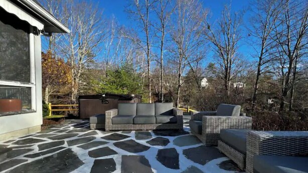 Un patio al aire libre con suelo de piedra, mobiliario de mimbre y un jacuzzi.