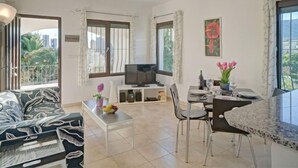 Amplia sala de estar con sofá, una mesa de comedor con sillas, televisor y balcón con vistas a la ciudad.