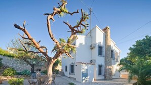 Una casa de dos pisos con fachada de piedra, camino de entrada de grava y un árbol en el patio delantero.