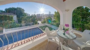 Un balcón con piscina, sillas blancas y una mesa con una botella y vasos.