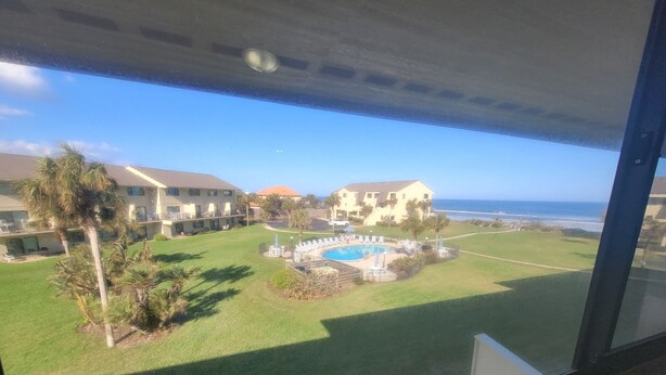 A view of a hotel courtyard with a swimming pool, palm trees, and a building with a red roof. - SH 149.Ocean View Townhouse with great pool and ocean view. (St. Augustine)