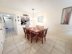 A dining area with a wooden table and chairs, a kitchen in the background, and a staircase leading to another room. - SH 149.Ocean View Townhouse with great pool and ocean view. (St. Augustine)