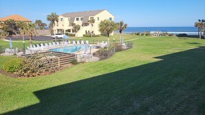 A pool area with lounge chairs and umbrellas, a building with a flat roof, and a view of the ocean. - SH 149.Ocean View Townhouse with great pool and ocean view. (St. Augustine)