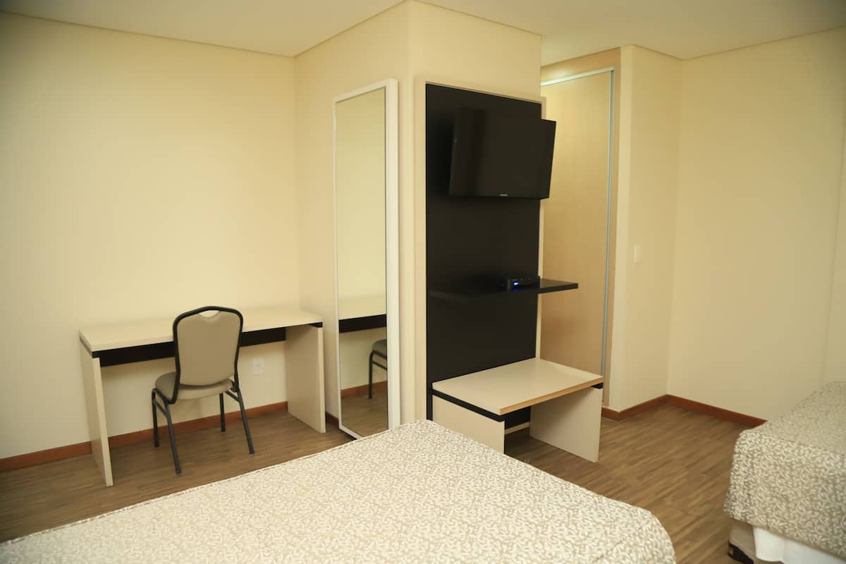 A hotel room with a bed, a desk with a chair, a wardrobe, and a television.