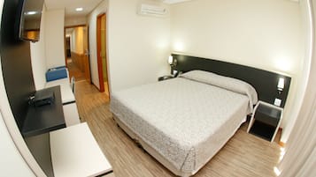 Habitación de hotel con cama, mesitas de noche, escritorio con silla, televisor y aire acondicionado.