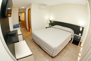 A hotel room with a bed, bedside tables, a desk with a chair, a TV, and an air conditioning unit. - Hotel Financial Ltda (Belo Horizonte)