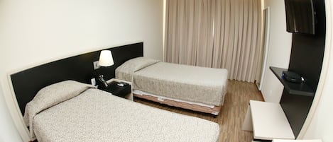 A hotel room with two beds, a desk, a TV, and a window with curtains.